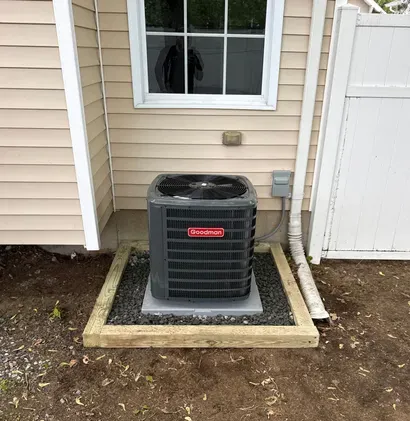 Outdoor air conditioner unit beside a house, surrounded by a small gravel and concrete border.