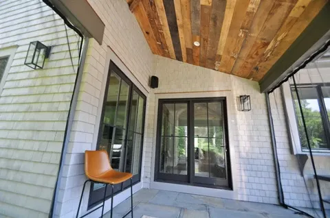 A back porch with a wood-planked ceiling, shingle siding, and large glass French doors.