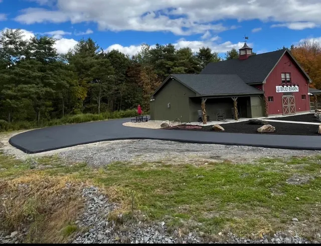 A red barn with a black roof is next to a green house