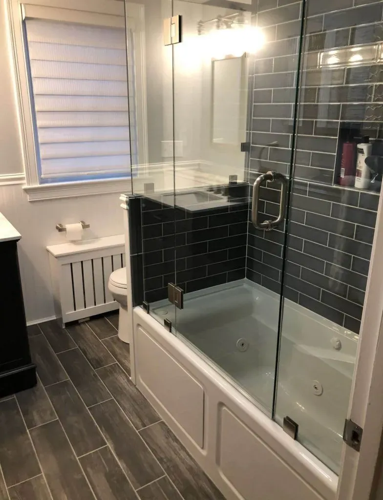 Modern bathroom with a glass shower enclosure, dark tiled walls, and white tub.