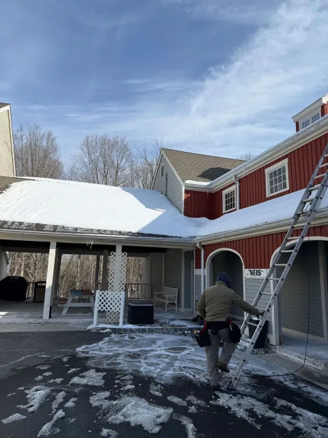 Person walking in a snowy courtyard beside a red building with a ladder leaning against it.