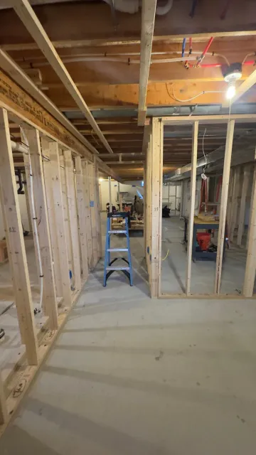 Basement under construction; wood framing walls, concrete floor, ladder, and exposed ceiling beams.
