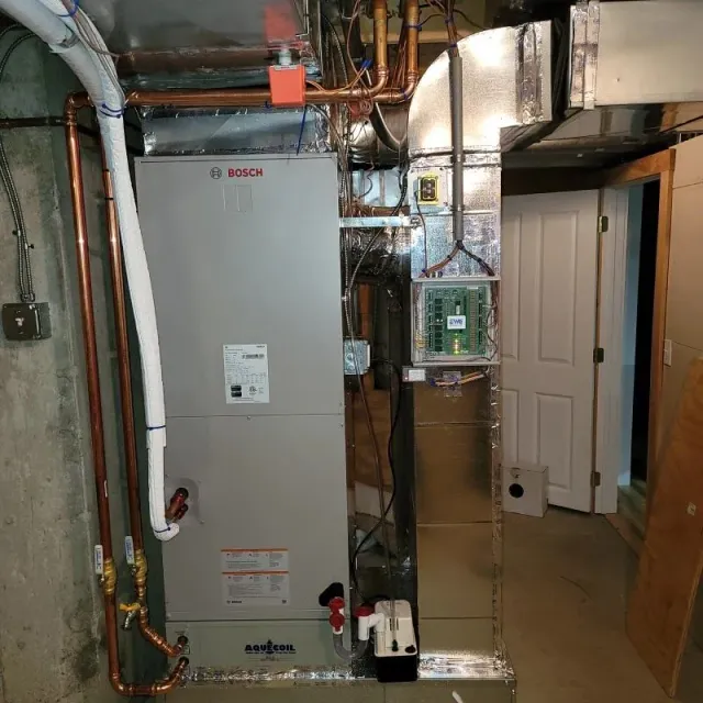 Furnace in a basement, with copper pipes, ductwork, and an electrical panel.