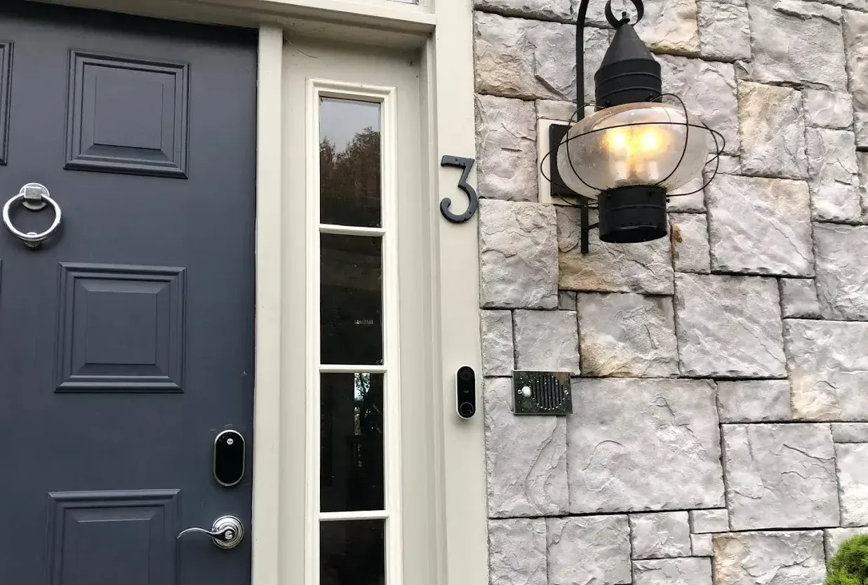 A newly installed outdoor electric globe lantern outside of a home with a blue door and a stone facade. a metal #3 on the door near a camera doorbell.