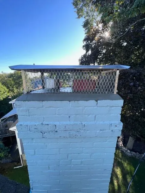 A white brick chimney with a metal cover on top of it.