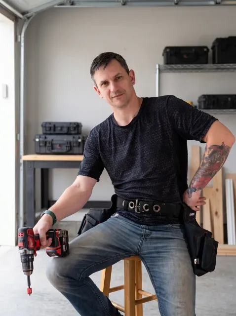 Ivan Grudin, founder and lead craftsman at BETEP, seated in a workshop with a drill and tool belt