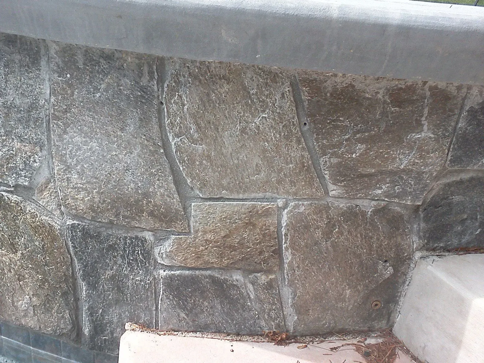 Stone retaining wall with irregular gray-brown stones and a concrete cap.
