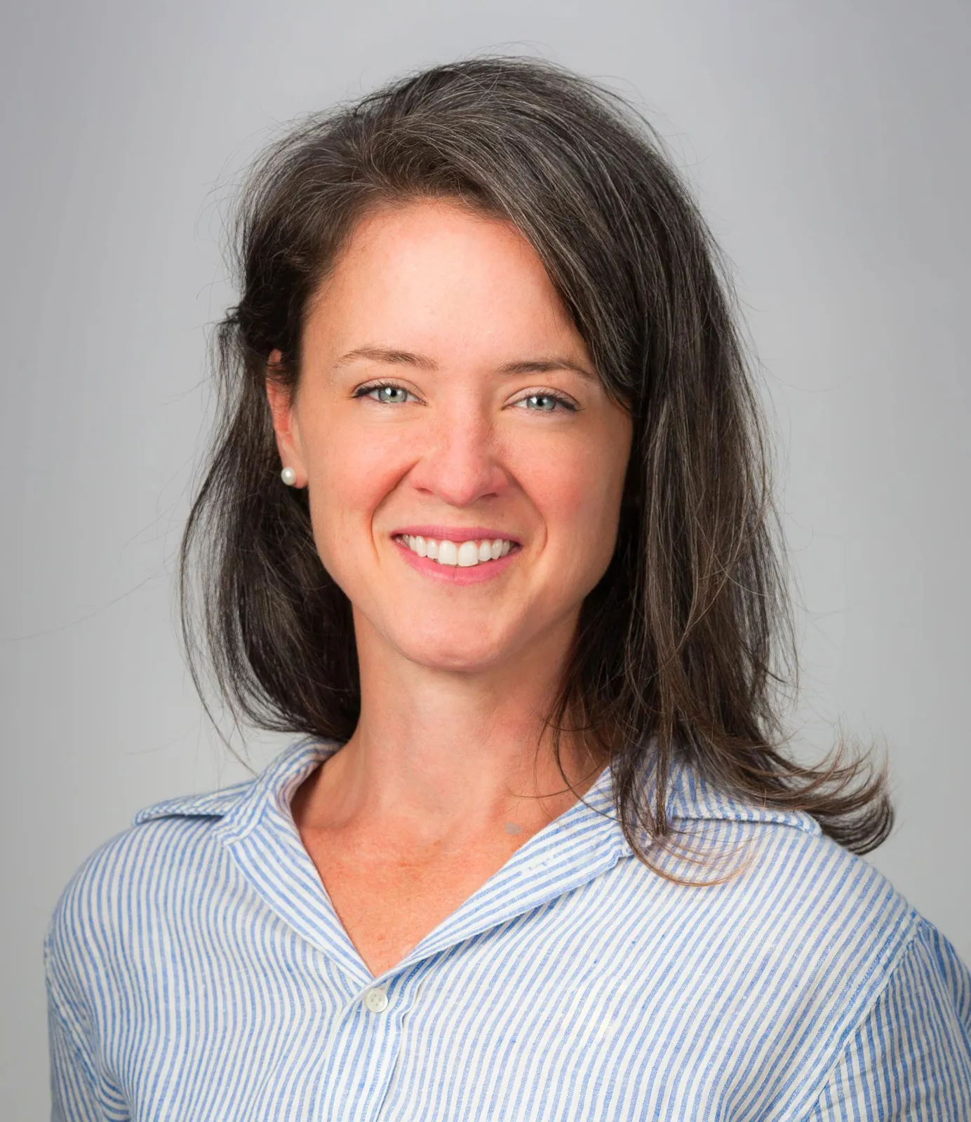 Woman with long brown hair, wearing a blue striped shirt, smiling against a plain light background—perfect for representing a professional commercial cleaning service.