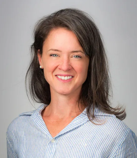 Woman with long brown hair, wearing a blue striped shirt, smiling against a plain light background—perfect for representing a professional commercial cleaning service.
