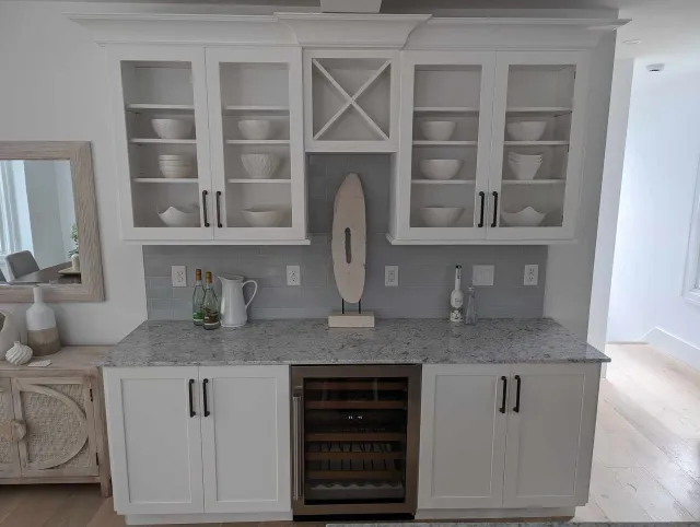 A kitchen with white cabinets, granite counter tops, and a wine cooler.