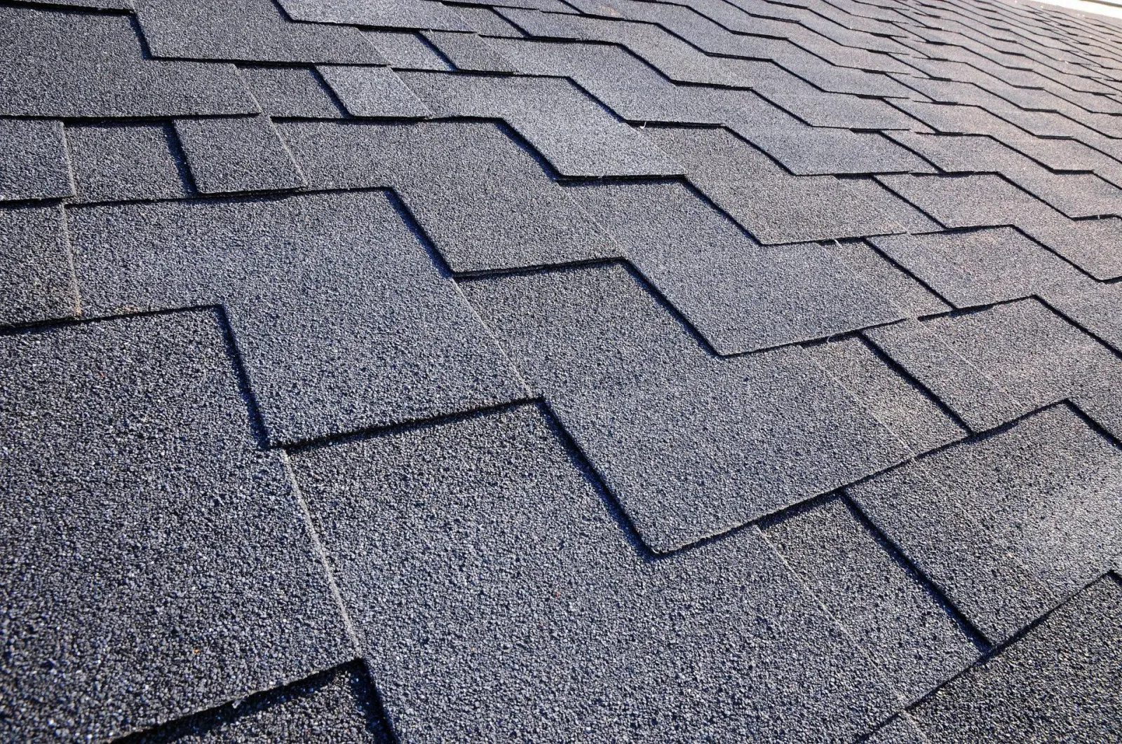 Close-up of asphalt shingle roof, dark gray color, zigzag pattern.