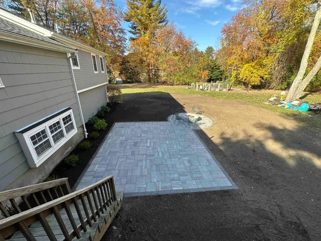 New paver patio installed beside a New England home with fresh loam and beds