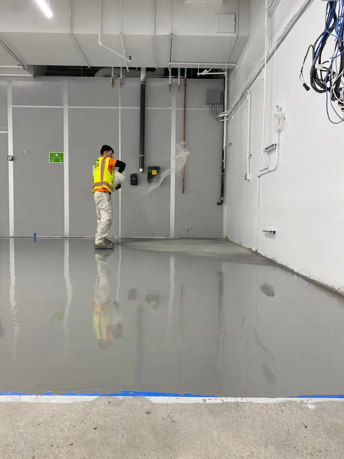 Worker in a yellow safety vest inspecting a glossy concrete floor in a large industrial room