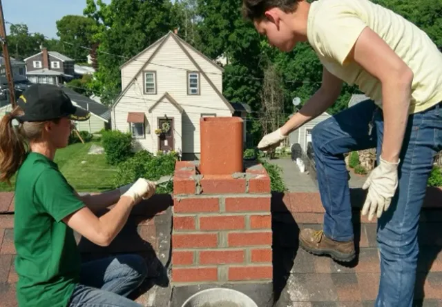 Northeast Chimney Sweeps team performing chimney masonry repair and repointing on a residential rooftop in Massachusetts.