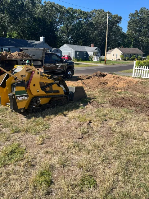 Yellow stump grinder on grass, truck in the background, residential setting.