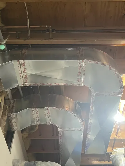 Installation of ductwork through a ceiling with insulation and piping visible, with reflective foil insulation covering the ducts.