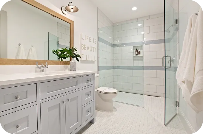 Gray vanity with white countertop, wooden-framed mirror, plant, and glass shower enclosure