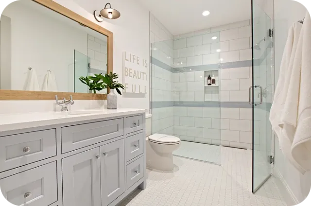Gray vanity with white countertop, wooden-framed mirror, plant, and glass shower enclosure