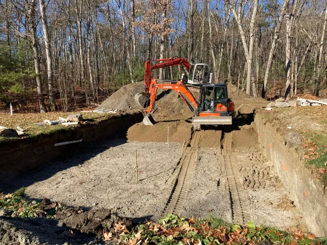 An excavator is digging a hole in the ground in the woods.