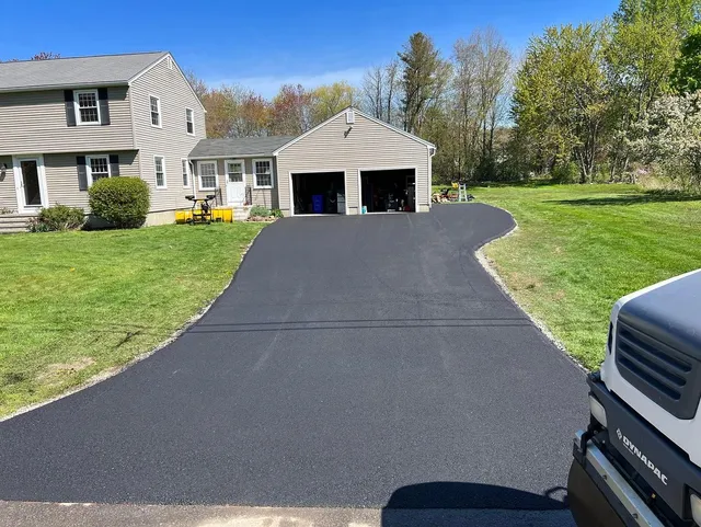 Black asphalt driveway leads to a two-car garage, flanked by green grass and a house.