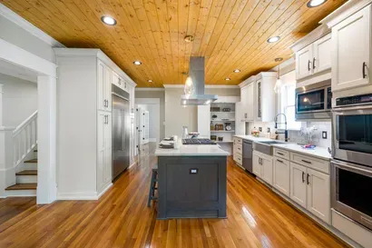 A modern kitchen featuring white cabinets, a dark gray island, stainless steel appliances, and a natural wood ceiling.