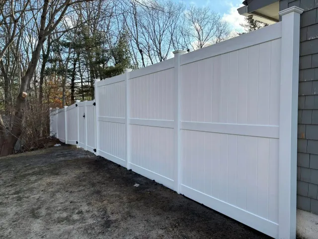 White vinyl privacy fence in a yard next to a gray building.