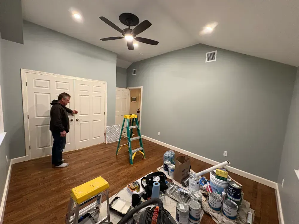 A person stands in a room with light blue walls and wood floors, touching closed double doors, with a ladder nearby.