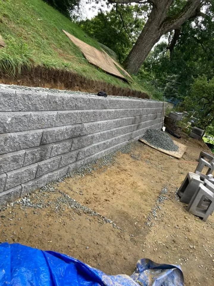 Segmental block retaining wall under construction on a sloped yard