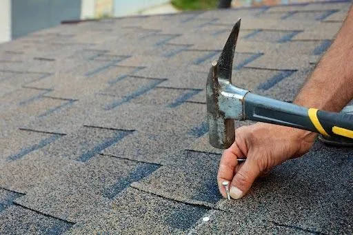Hammer hitting a nail on a shingled roof, securing it.