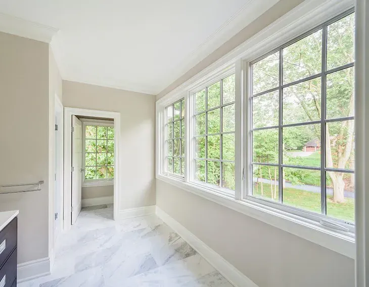 Bright white hallway with large windows, marble floor, and a view of green trees outside