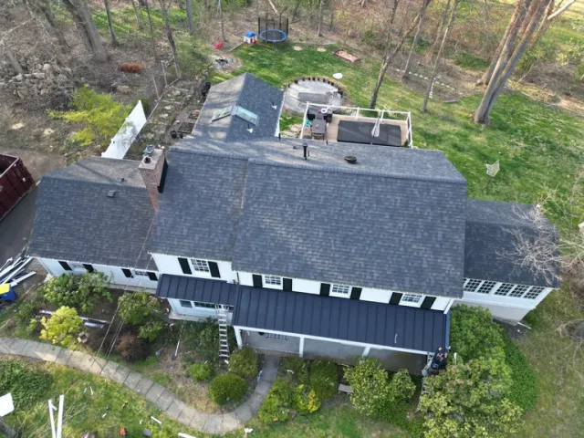 Aerial view of a modern black and white residential home with gray roof surrounded by tall trees and forest landscape