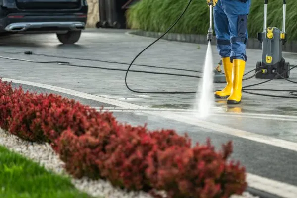 Homeowner Power Washing Residential Driveway Using Pressure Washer.