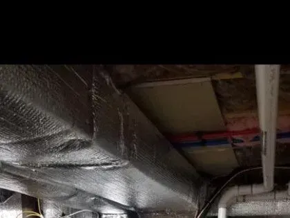 Foil-wrapped ductwork and exposed pipes in a dim ceiling crawlspace