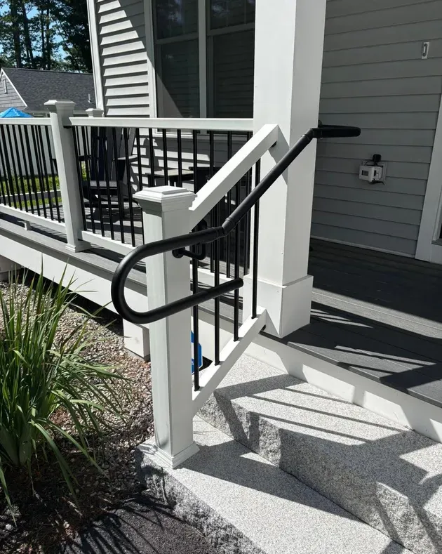 Front porch steps with white posts and black handrails beside a gray house entrance