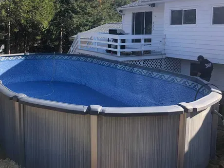A large swimming pool is sitting in front of a house.