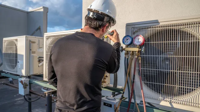 A man is working on an air conditioner on the roof of a building.