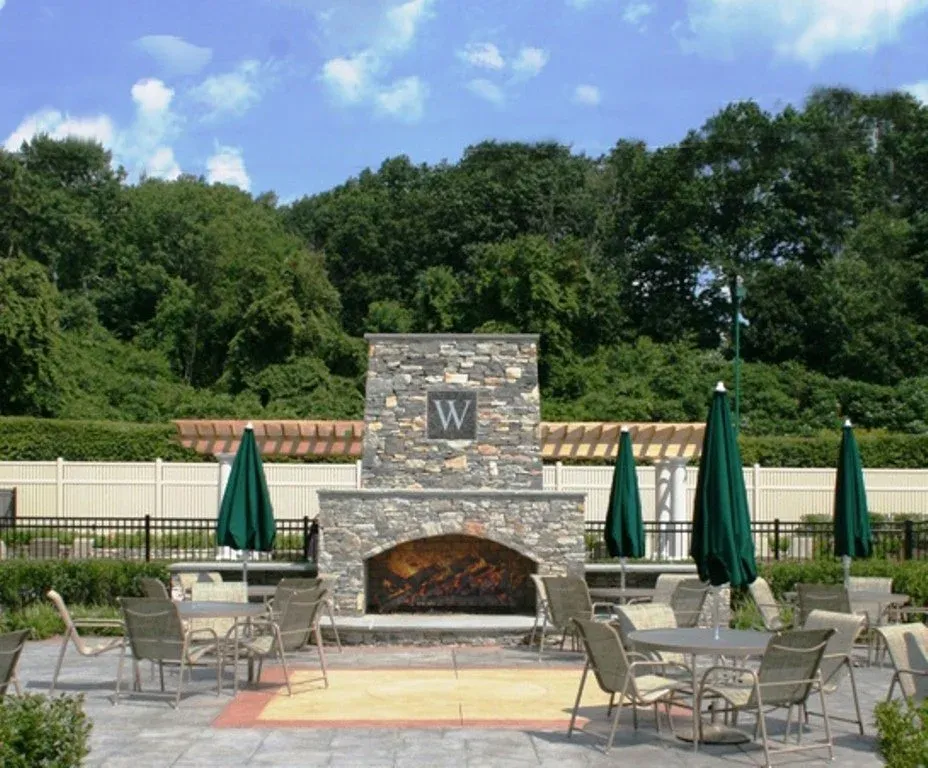 Outdoor patio area with stone fireplace featuring the letter 'W', surrounded by tables, chairs, and closed green umbrellas.