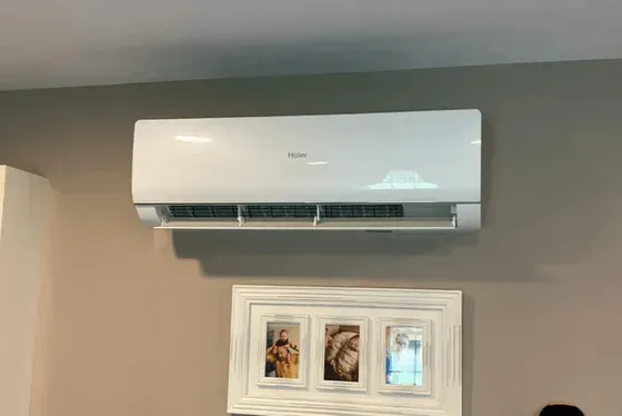 A white air conditioner is hanging on a wall next to a picture frame.