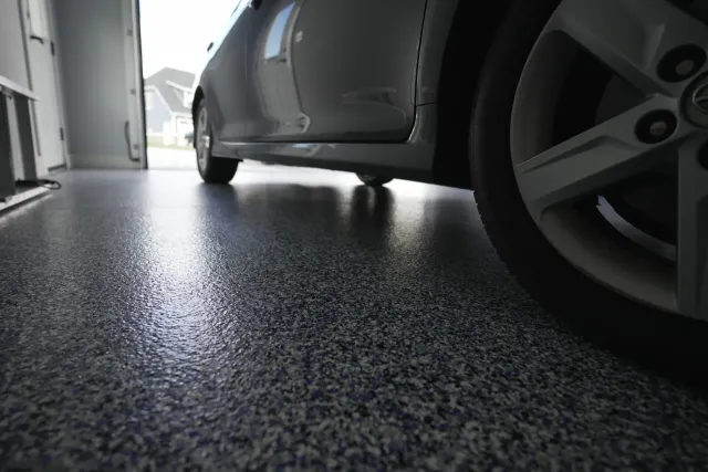 Car in an open residential garage that is sealed with blue white and gray premium and professional epoxy vinyl chip floor.