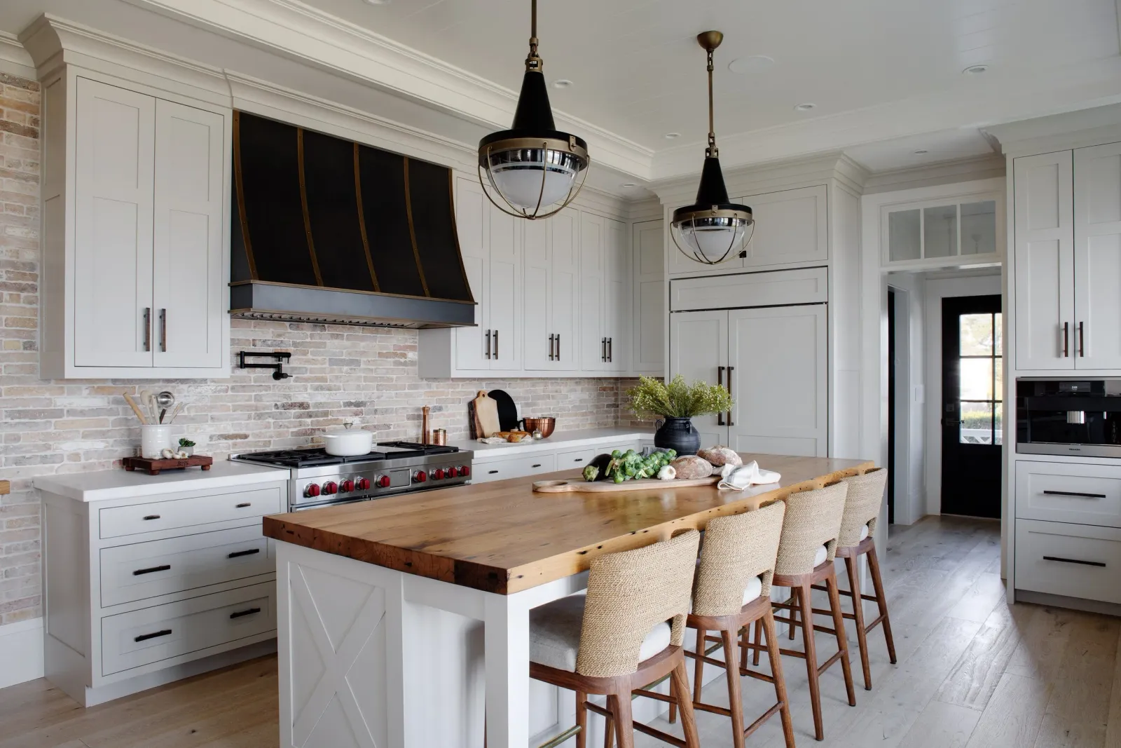Hardwood floor installation in a Marshfield kitchen with white cabinets, a brick backsplash, a wooden island with seating, a black and brass stove hood, and two black pendant lights.