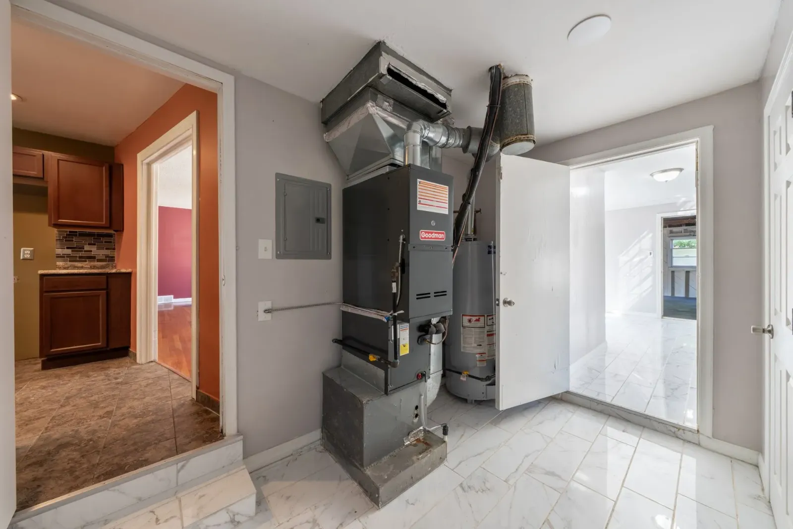 Small utility room with a furnace, white tile floor, and open door to a kitchen and another bright room