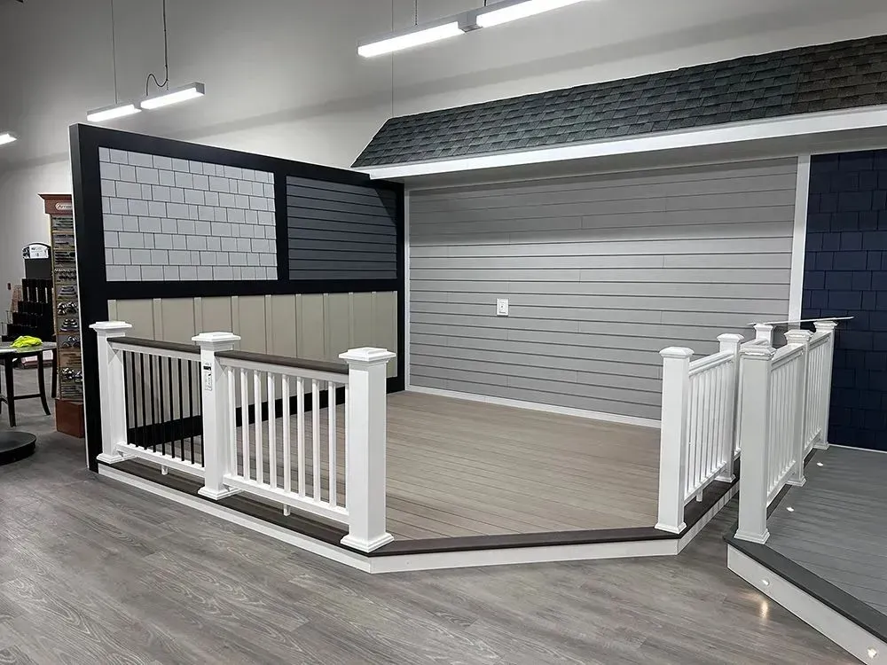 Deck display with railing and siding samples. Light brown deck, white railing, gray and blue siding.