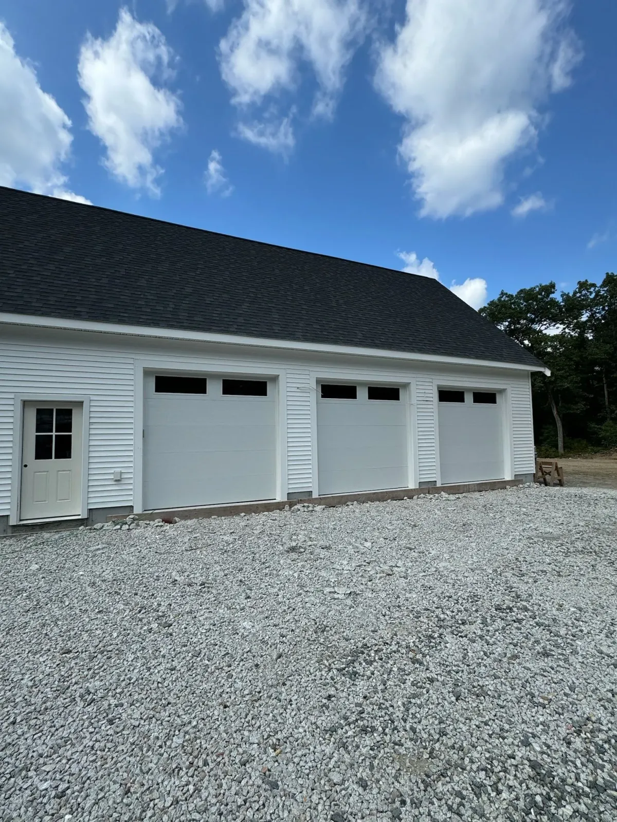 A white garage with three garage doors and a gravel driveway