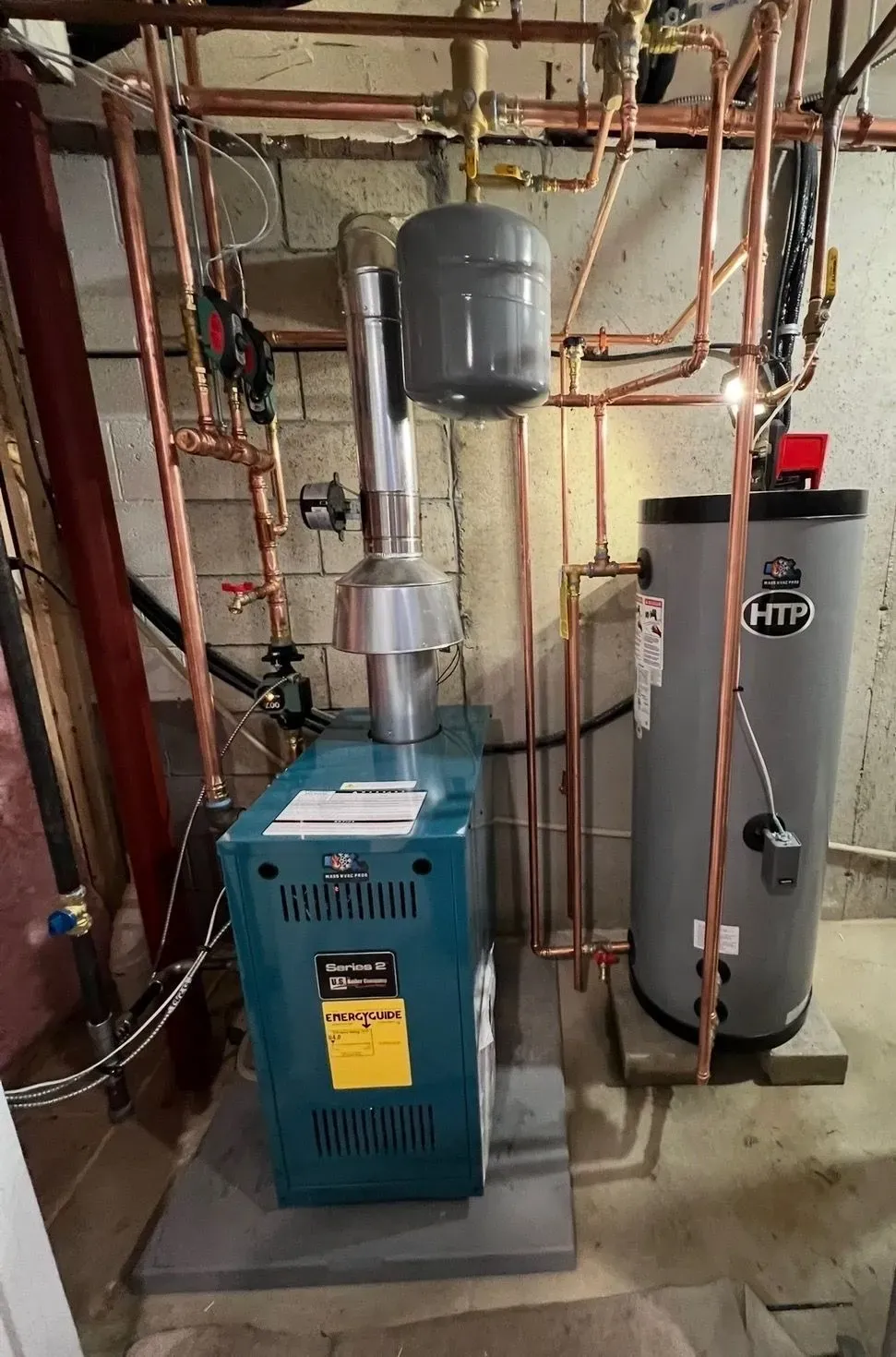 Basement utility room with furnace, water heater, and exposed pipes on a concrete floor.