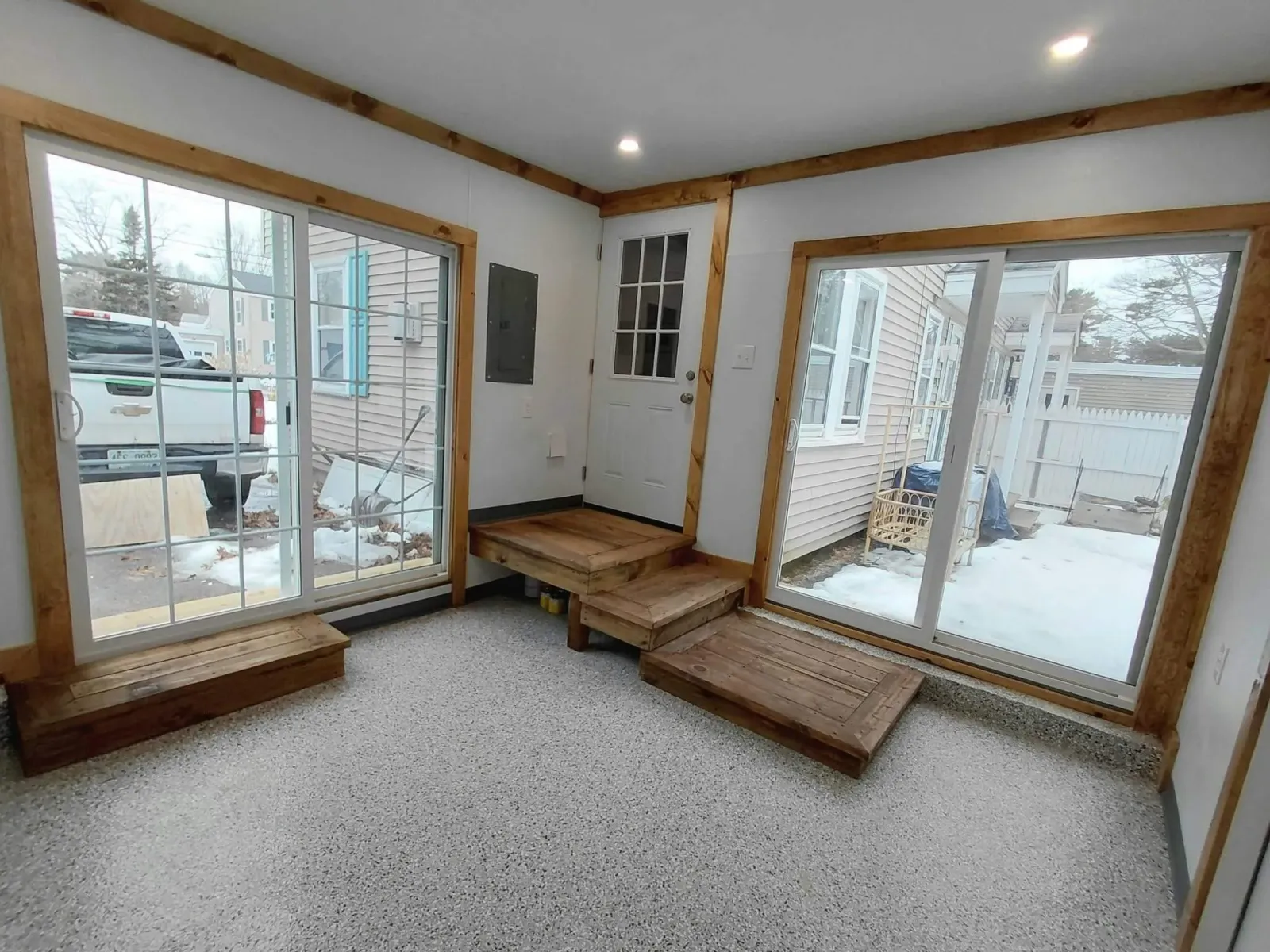 Room with speckled floor, wooden trims, a white door with glass panes, and two large sliding glass doors.