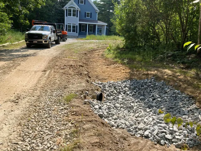 A truck is parked on the side of a dirt road in front of a house.