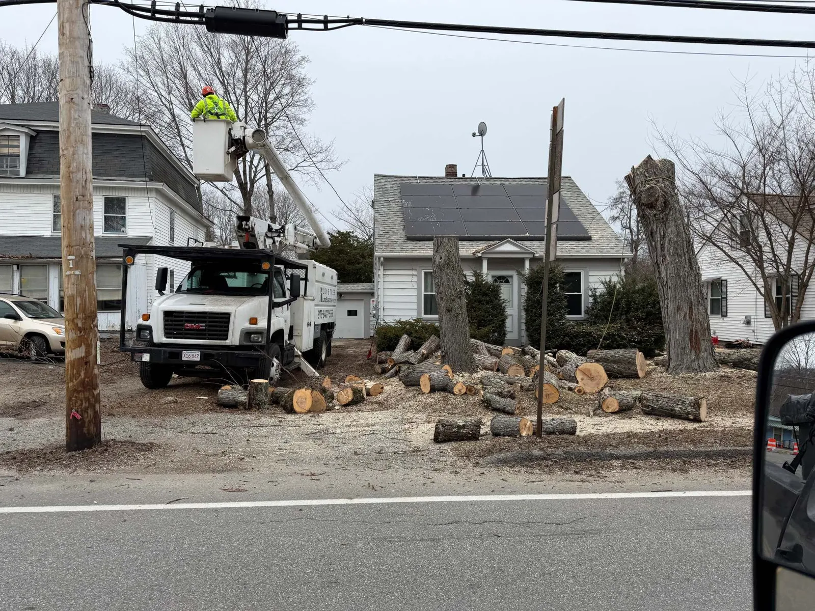 Tree-trimming crew in a bucket truck clearing debris beside a residential street after storm damage