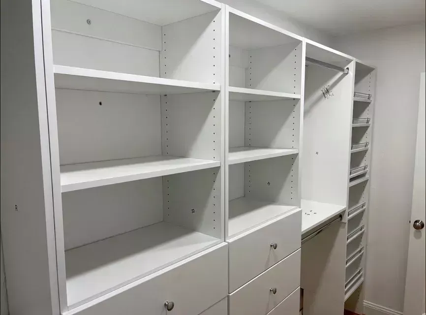 White built-in closet shelving with open cabinets and drawers in a narrow hallway.