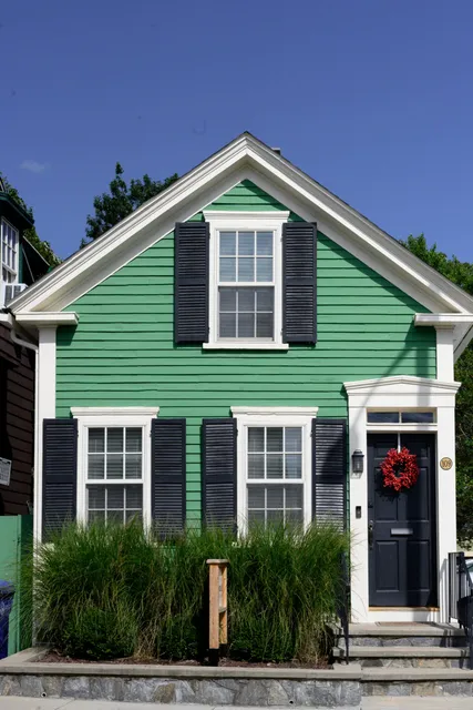 Green house exterior with dark shutters, a red wreath, and house number 109