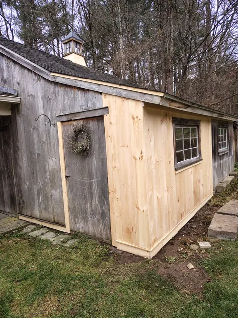 A wooden shed with a newly added light wood extension.